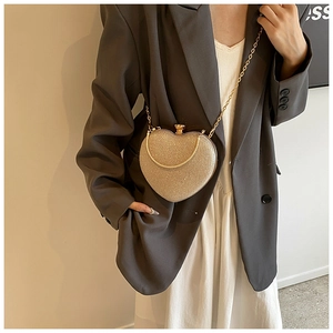 Dettaglio borsa a cuore glitterata oro con tracolla indossata su blazer grigio