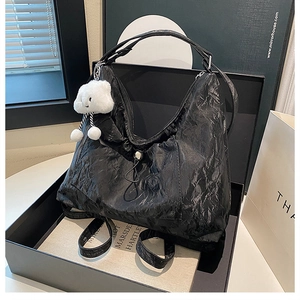 Detail view of black pleated PU leather tote bag with cute white cloud plush pendant decor