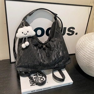 Black paper-texture pleated hobo bag with cute white cloud charm in urban scene
