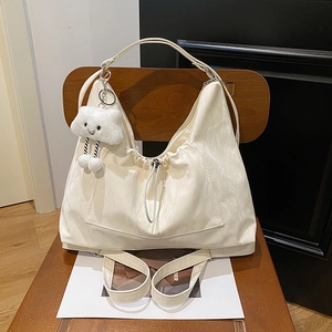 Elegant cream drawstring shoulder bag with a cloud pendant on a dark wooden chair