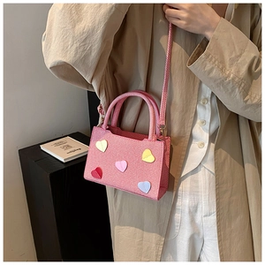 Détail d'un sac bandoulière tissé rose avec écussons en forme de cœur et poignées