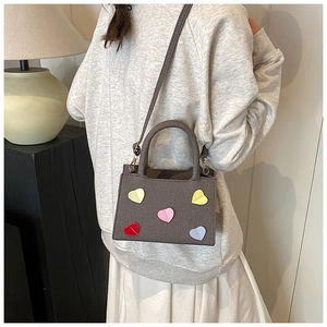 Detailed view of grey textured mini handbag with colorful heart patches on a woman's shoulder