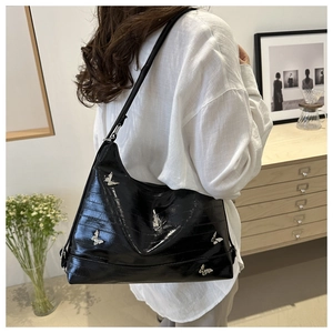 Close-up of black glossy shoulder bag with silver butterfly metal accessories on plain shirt