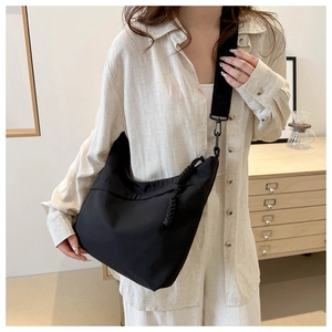 Detail view of a black nylon crossbody hobo bag with wide strap and woven zip pullers