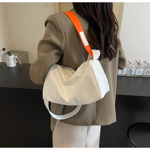 White crescent leather shoulder bag with vibrant orange strap shown on a brown suit jacket