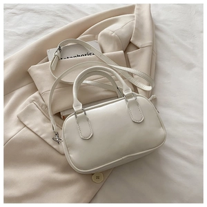 Détail d'un sac Boston minimaliste en cuir crème avec des poignées rondes sur fond neutre