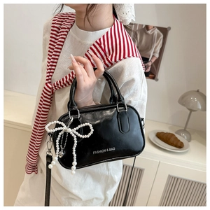 Detail of black glossy leather satchel featuring a pearl bow charm and logo lettering