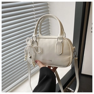 Detailed shot of a white fashion handbag featuring a pearl bow charm and adjustable strap