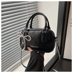 Detail of glossy black handbag with pearl bow charm and elegant hand-held strap