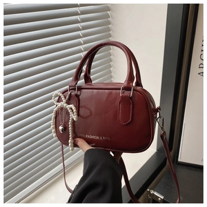 Detail of burgundy glossy Boston bag with pearl bow charm and silver heart pendant