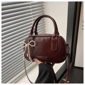 Detail of burgundy PU leather handbag with pearl bow charm and metal zipper