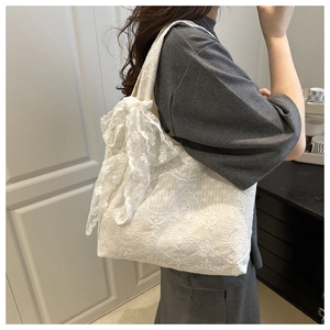 Detail of white lace tote bag featuring intricate floral patterns and a large side bow