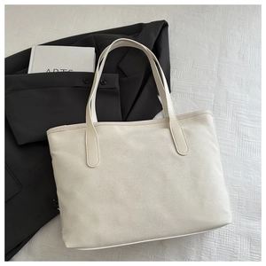 Top-down view of cream minimalist tote bag on fabric with book and blazer backdrop