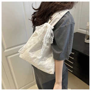 Close-up of white floral lace tote bag with delicate bow knot detailing on a shoulder strap