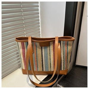 Détail d'un sac cabas en paille tressée aux rayures colorées et anses en cuir fin