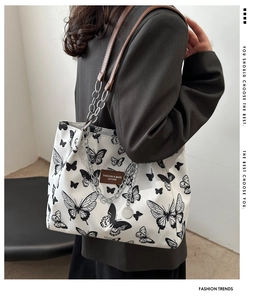 Detail of canvas tote bag showing black butterfly prints and brown leather chain straps