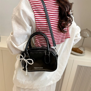 Fashionable black Boston pillow bag with pearl bow charm and crossbody strap on a model