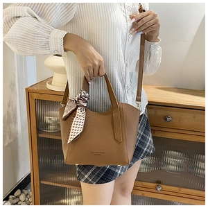 Détail du sac à main en cuir marron grainé avec foulard décoratif et finitions dorées