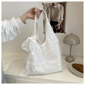 Detail of white lace tote bag with floral embroidery and decorative bow handle