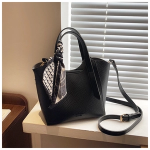 Détail du sac seau en cuir noir grainé avec foulard géométrique sur la poignée