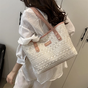 Chic beige straw tote bag with pink leather handles and gold rivet accents on a shoulder strap