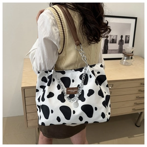 Detail of cow print canvas tote with brown leather strap and silver chain accent