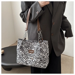 Detail of zebra pattern tote bag featuring brown leather handles and silver chain accents