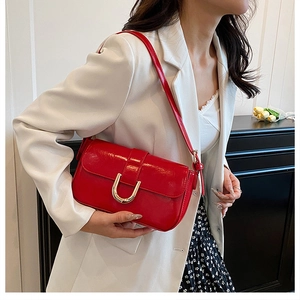 Detail of red crossbody bag with golden U-shaped buckle on elegant white suit
