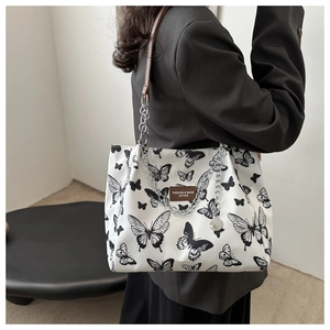 Detail of white canvas tote bag with butterfly prints, metal chain and leather strap