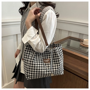 Detail of houndstooth tote bag featuring brown leather handles and silver chain metal charm