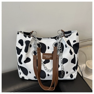 Close-up of cow print canvas tote bag with brown leather handles and metal chain