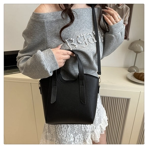 Detail of black pebbled leather handbag with dual handles and slim shoulder strap