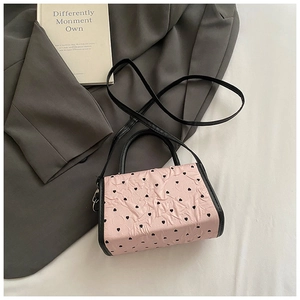 Detail view of pink heart-patterned shoulder bag with black strap on a textured surface
