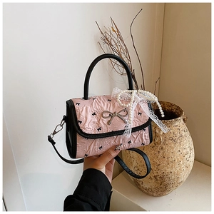Detail of light pink pleated handbag featuring silver bow buckle and pearl lace charm