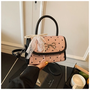 Close-up of pink heart-print handbag with lace bow and pearl chain details