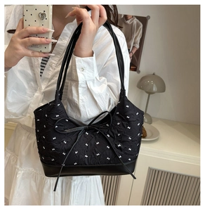 Close-up of black quilted shoulder bag featuring white bow patterns and bow detail