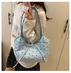 Close-up of light blue tote bag with embossed pattern and black bow embroidery detail