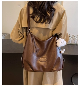 Detail of brown hobo bag with glossy leather texture and white plush cloud charm