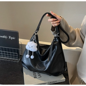 Detail of black faux leather tote bag with white cloud plush charm and adjustable strap