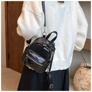 Detail of a chic black glossy patent leather mini backpack with silver zippers on model