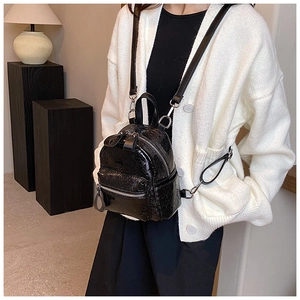 Detail of black mini leather backpack with silver zippers and glossy texture finish
