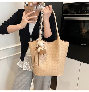 Detail der beige geflochtenen Ledertasche mit süßem Bärenanhänger in wohnlicher Umgebung