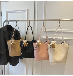 Detail von vier gewebten Tragetaschen in Khaki, Schwarz, Rosa und Beige mit Bärenanhänger