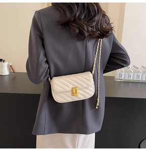 Quilted cream crossbody bag with gold chain strap shown on a model in a minimalist room