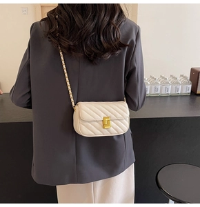 Close-up of quilted beige crossbody bag with gold lock and chain strap on grey blazer