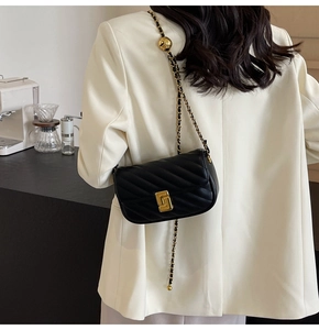 Detail of black quilted leather shoulder bag with gold hardware worn by a model