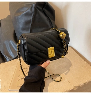 Detail of black quilted chain bag featuring V-stitch pattern and gold metal ball buckle