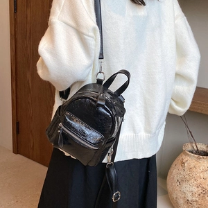 Chic black shiny leather mini backpack with silver zippers worn by a female model