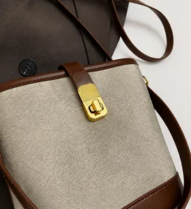 Close-up of golden metal clasp with brown leather trim on a textured fabric bucket bag