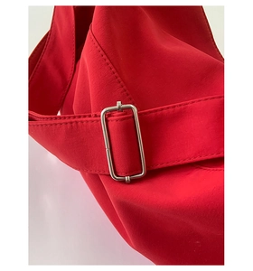 Detail showing the adjustable silver metal buckle on a red canvas shoulder bag strap